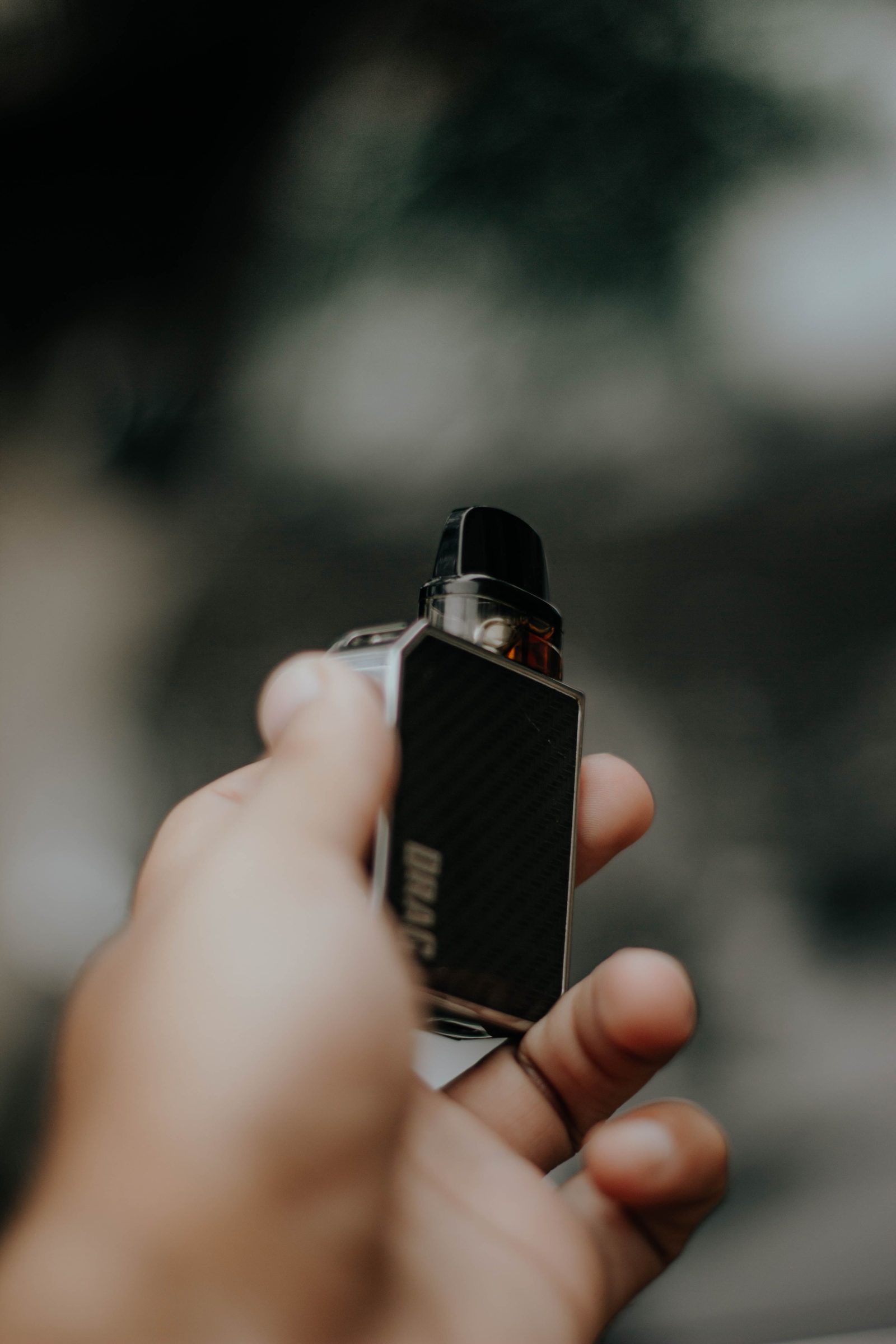 A hand holding a compact black vape device against a soft blurred background.
