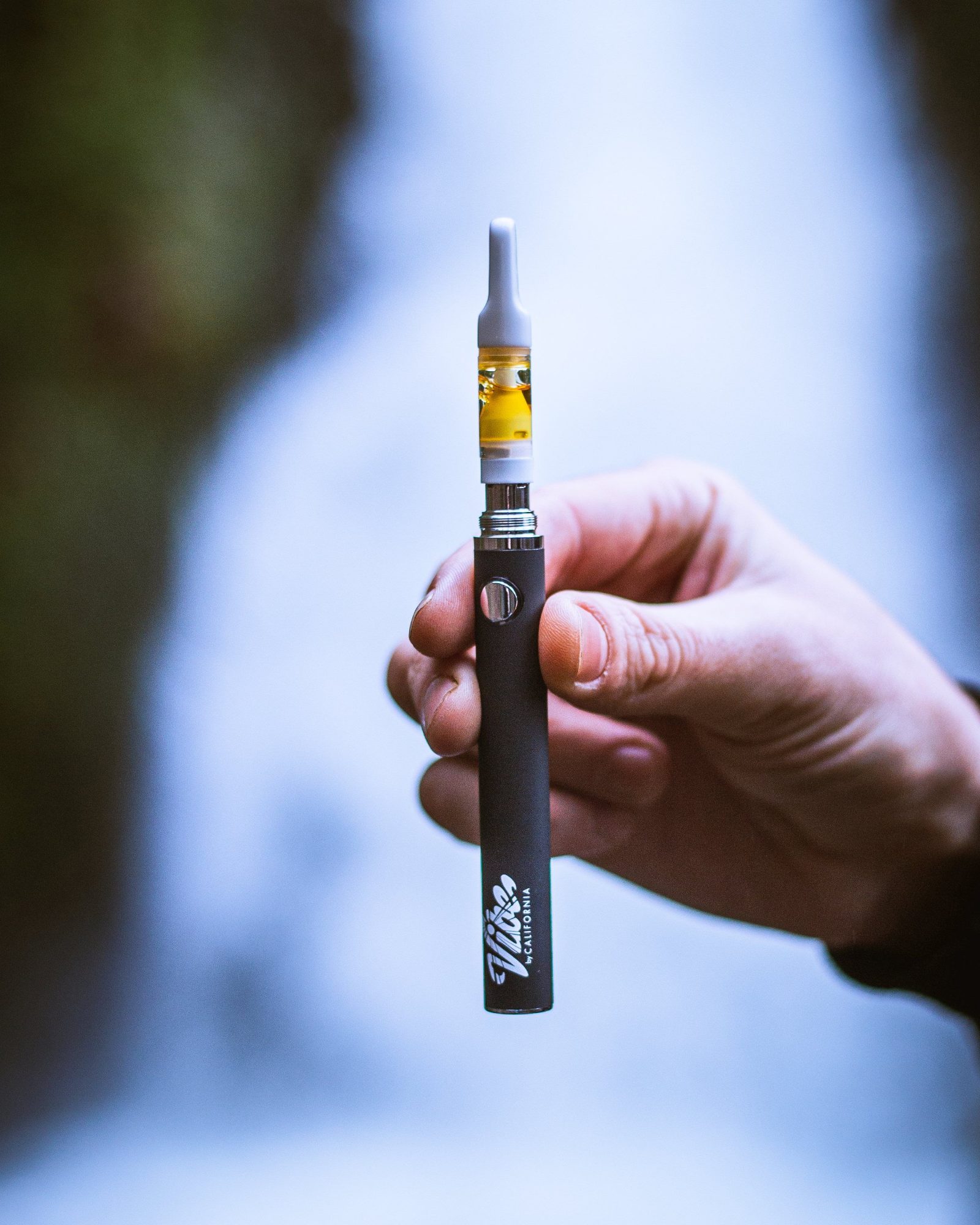 A hand holding a slim vape pen fitted with a gold cannabis oil cartridge.