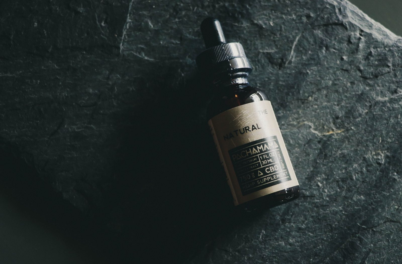 A dark glass cannabis oil bottle resting on a slate surface.