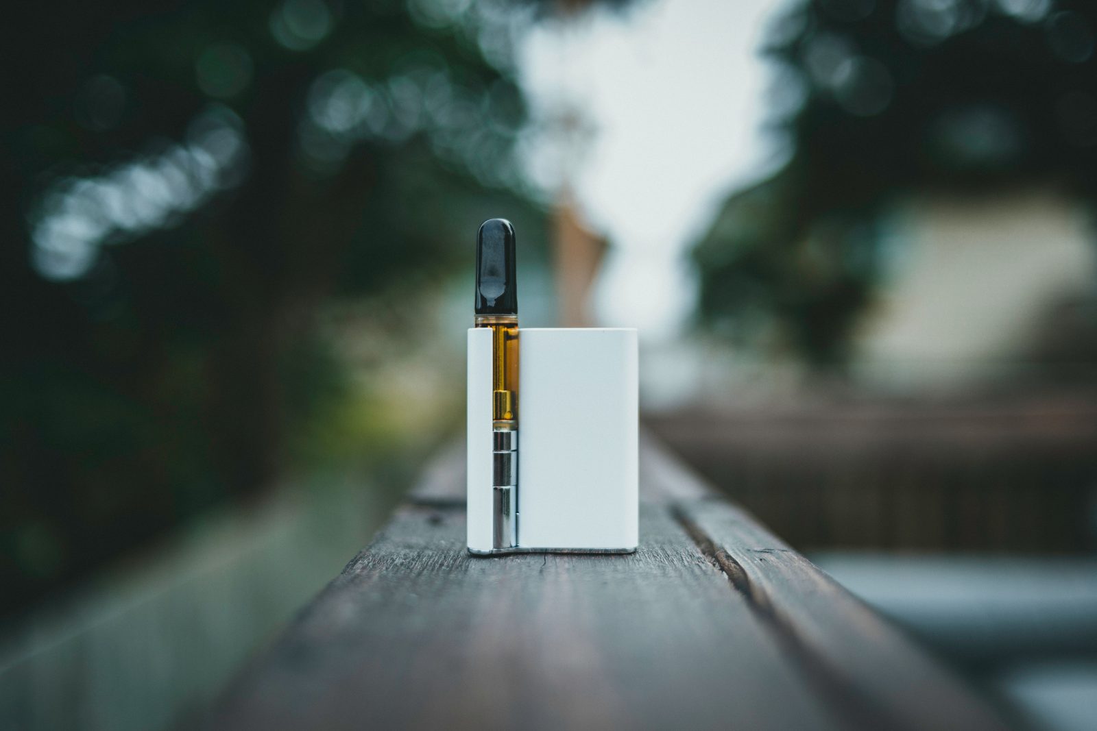 A cannabis vape pen fitted with an amber oil cartridge standing on a wooden surface.